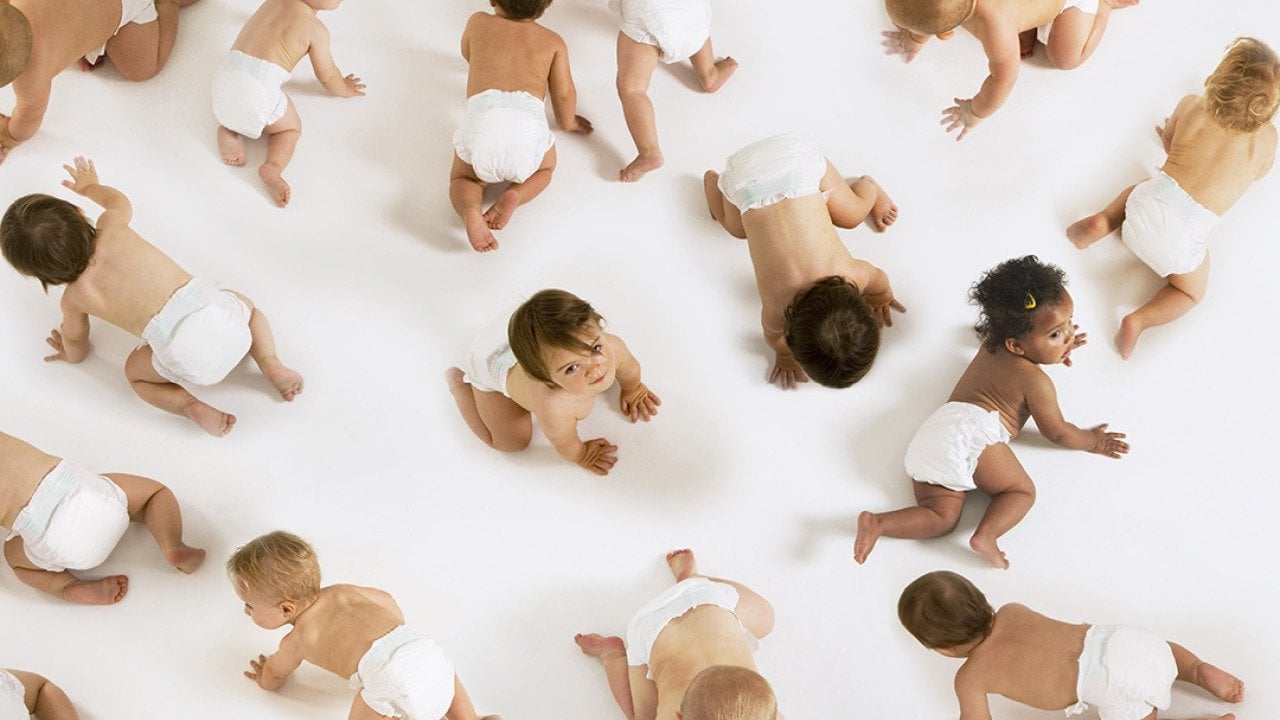 A group of diverse babies crawling on a white floor.
