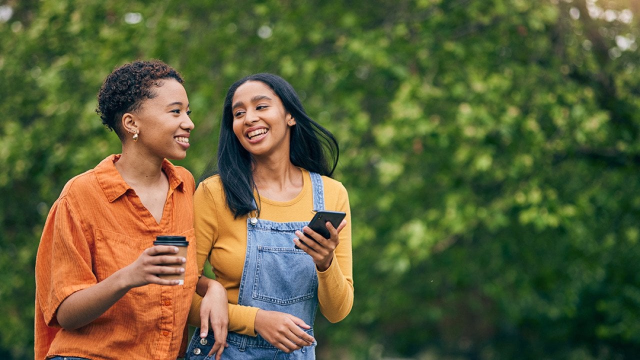 Two women having coffee while walking in a park.
