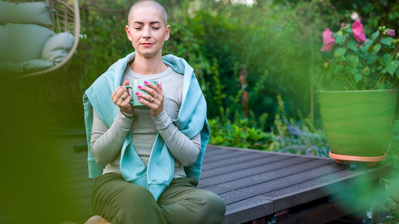 A breast cancer patient sitting on a garden patio with a cup of coffee in her hands.