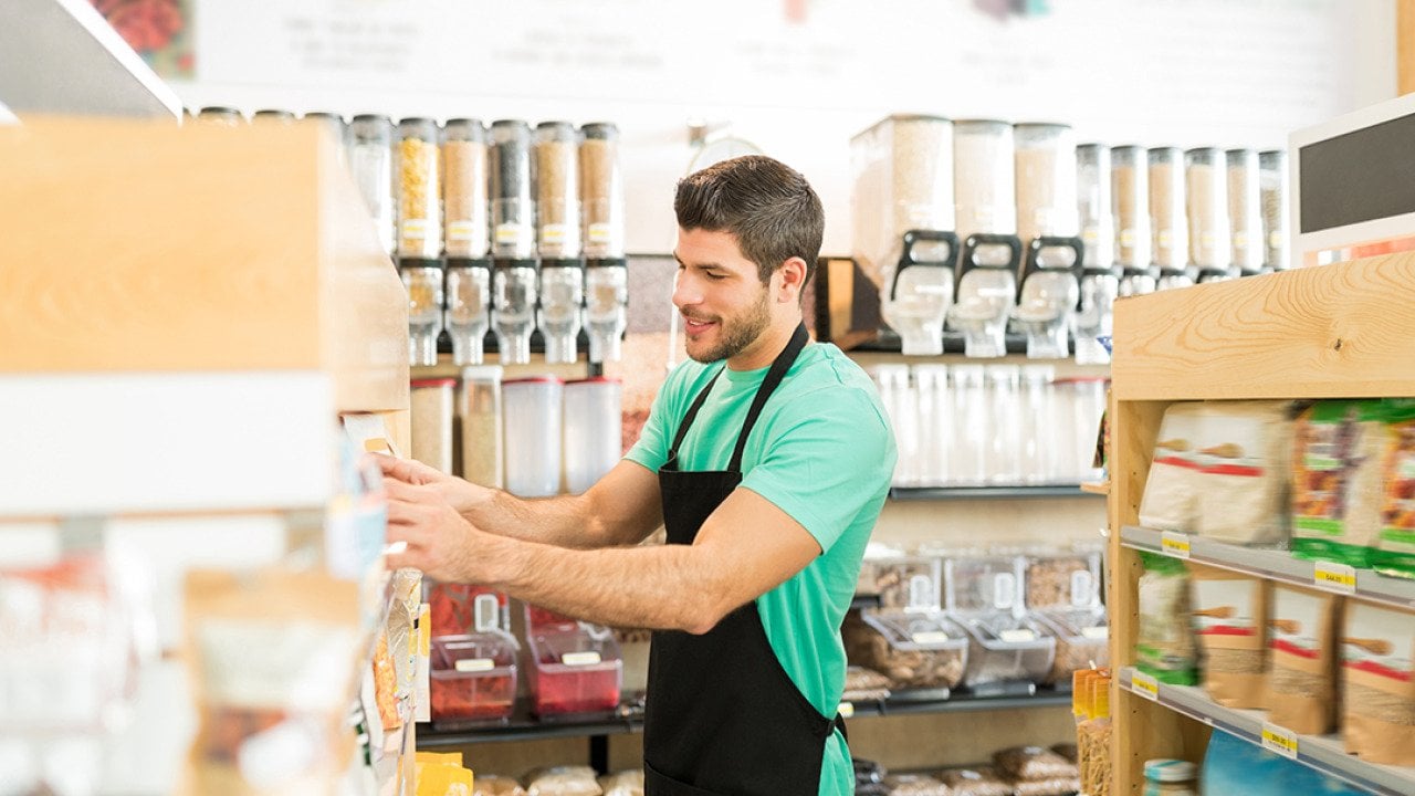 A zero-waste grocery store owner arranging stock of items on shelves.