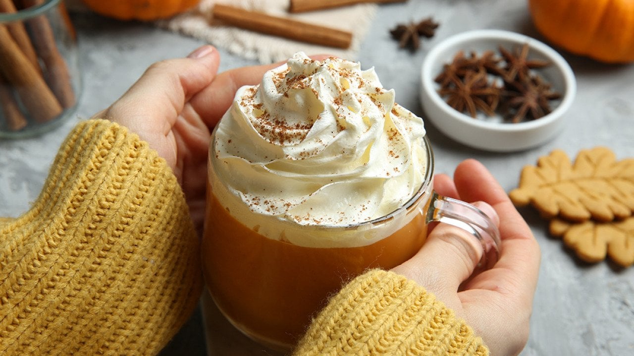 Closeup on a woman holding a cup of pumpkin spice latte with whipped cream.