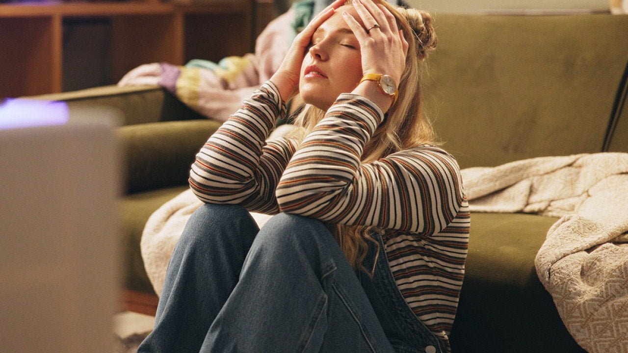 A stressed young woman sitting on the floor holding her head.