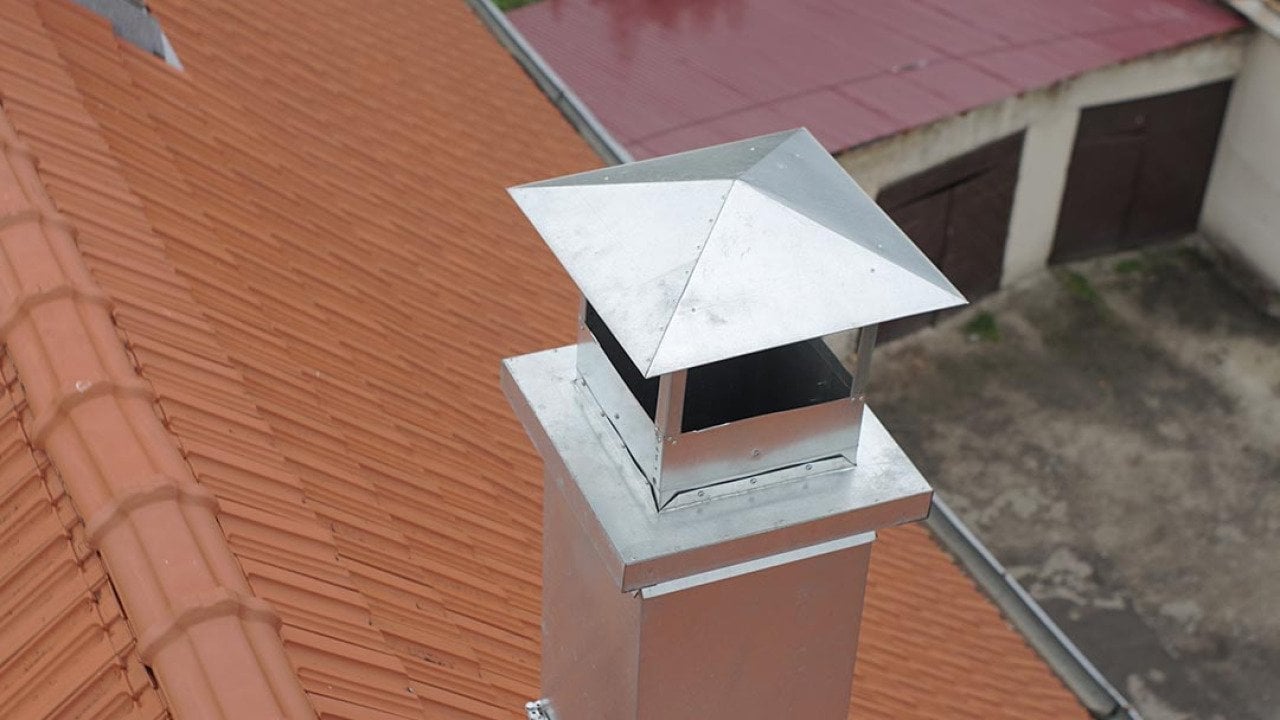Aerial view of metal pipe chimney with cap on a Spanish tile roof.                          