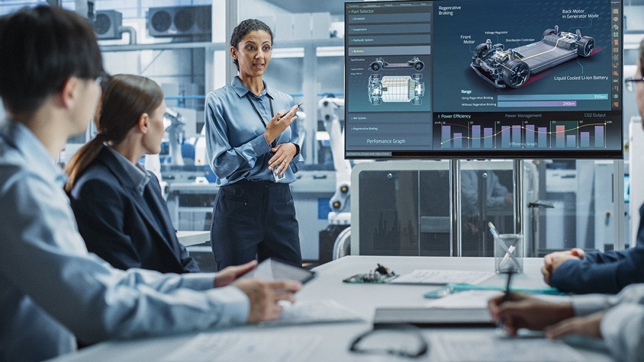 A female project manager leads her team of engineers with a presentation of a new car model in an EV manufacturing facility office.