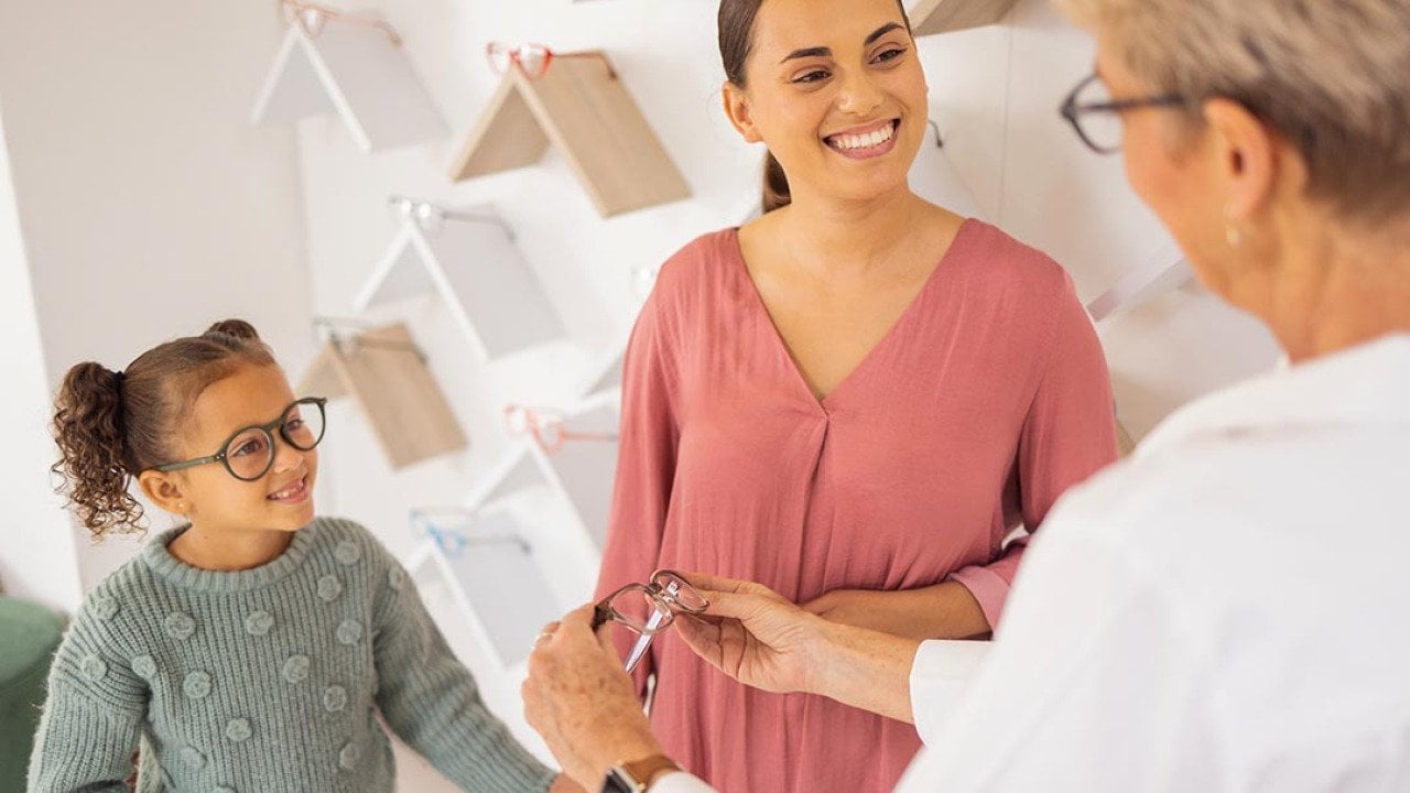 Girl with mother trying on glasses at an eyewear store talking to specialist. 