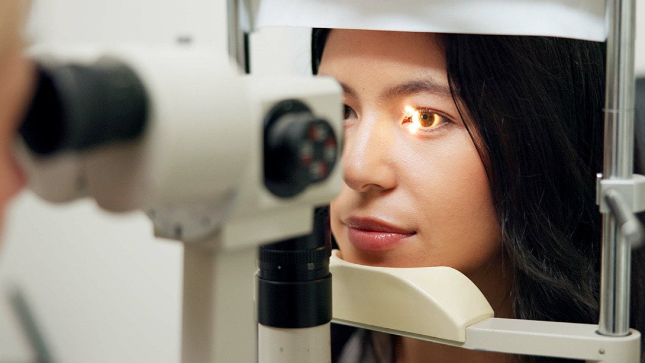 A woman in front of a slit lamp as an eye specialist takes her vision test.