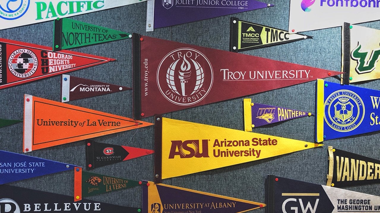 Pennant flags of US colleges and universities on a wall.