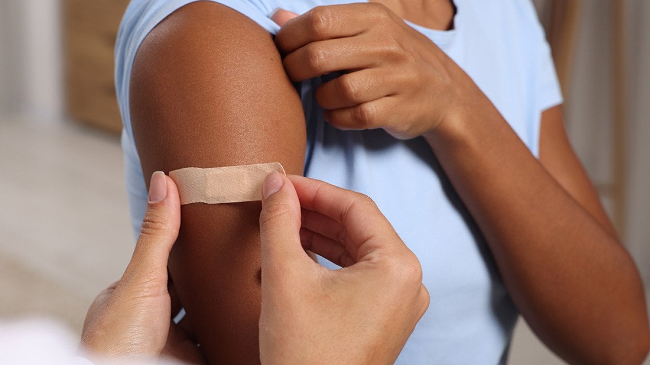 A doctor puts adhesive bandage on a woman's arm after vaccination.