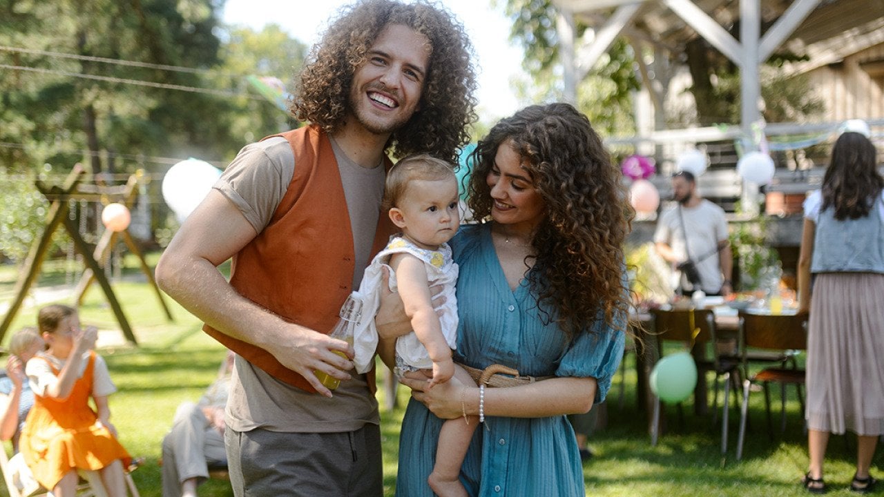 A happy couple pose with their baby at a backyard party.