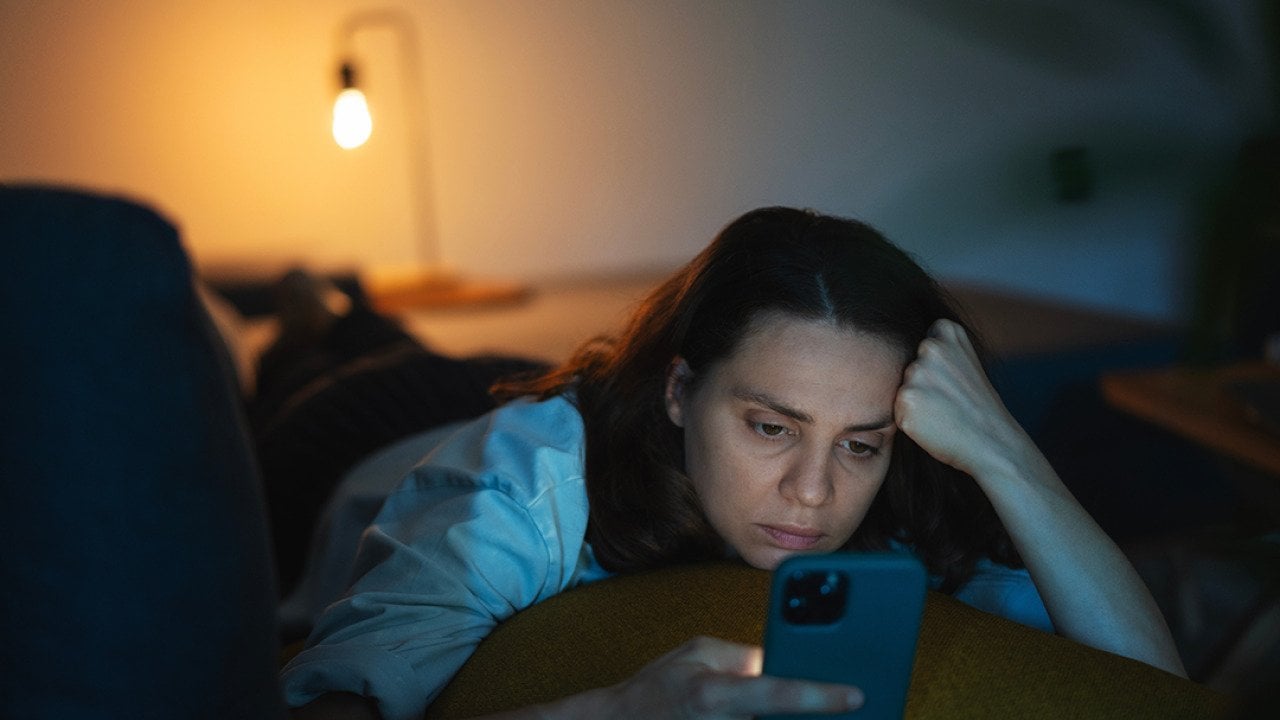 A serious young woman lying on a sofa and scrolling through her phone.