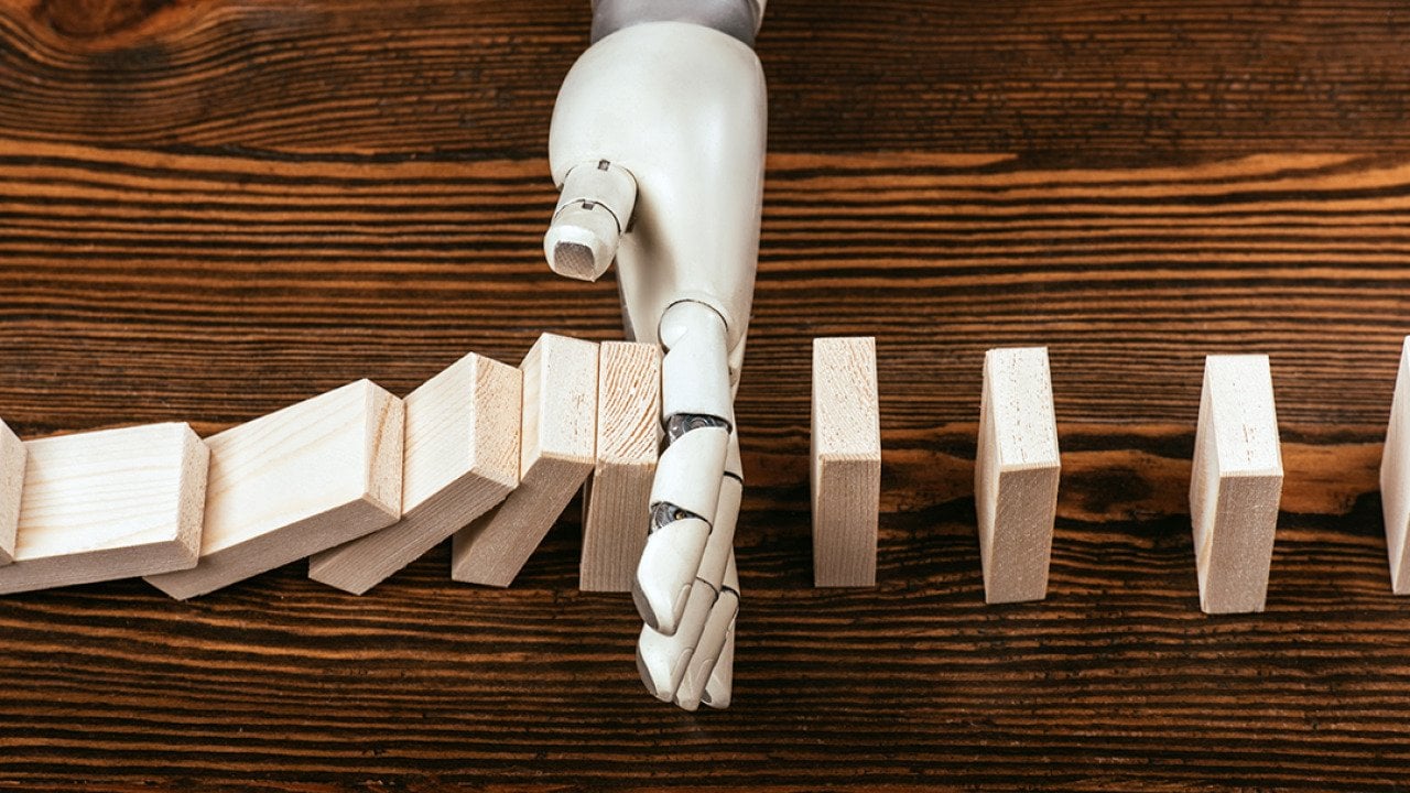 A robotic hand prevents wooden domino blocks from falling midway.