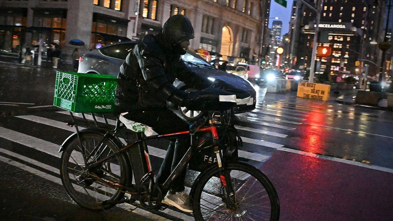 A rider transports a delivery using an e-bike on a street in midtown Manhattan on a rainy night on December 22, 2024 in New York City, USA.