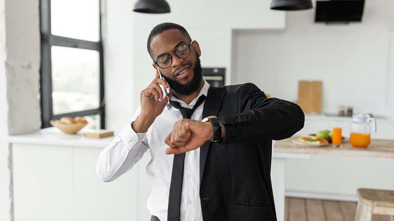 A black businessman on the phone looks at his wrist watch as he gets ready to go to work in the morning.