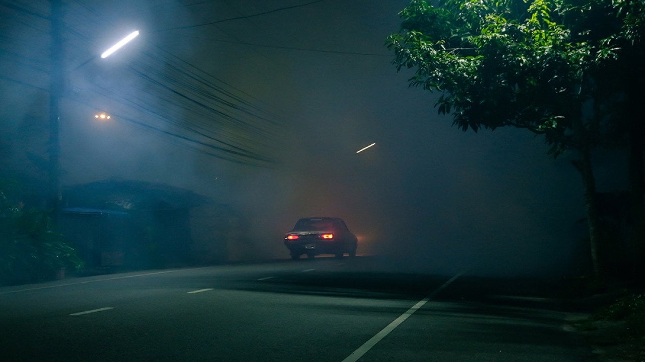 A classic car drives down a spooky road at night.