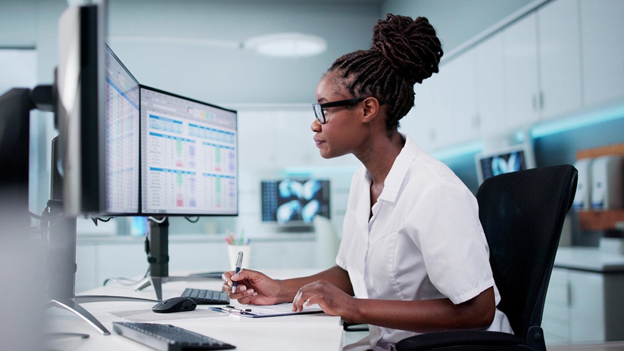 A hospital staff looking at spreadsheets and billing codes using desktop with multiple monitors.