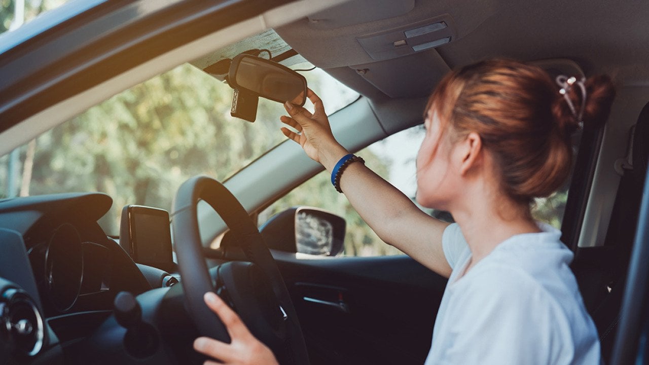 A woman adjusts her car's rearview mirror before driving.