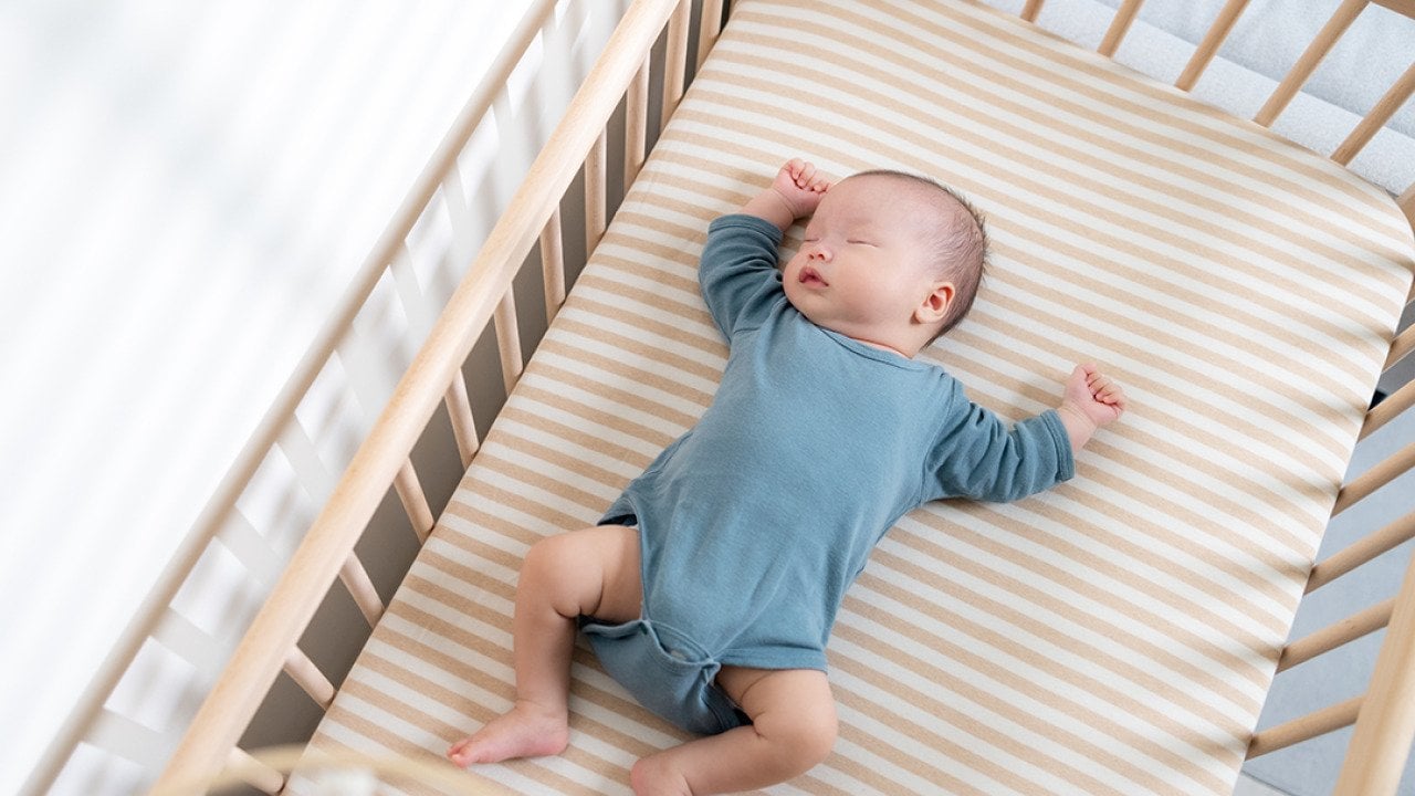 An infant quietly sleeps in a crib.