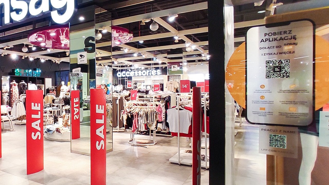 A clothing store having a sale in a shopping mall with a QR code system displayed at the entrance.
