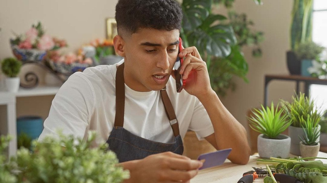 A flower shop business owner holding a credit card while talking on the phone.