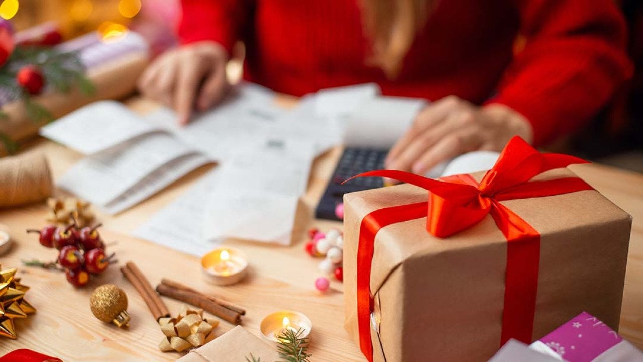 A woman calculates expenses on a table with holiday gifts and decorations.