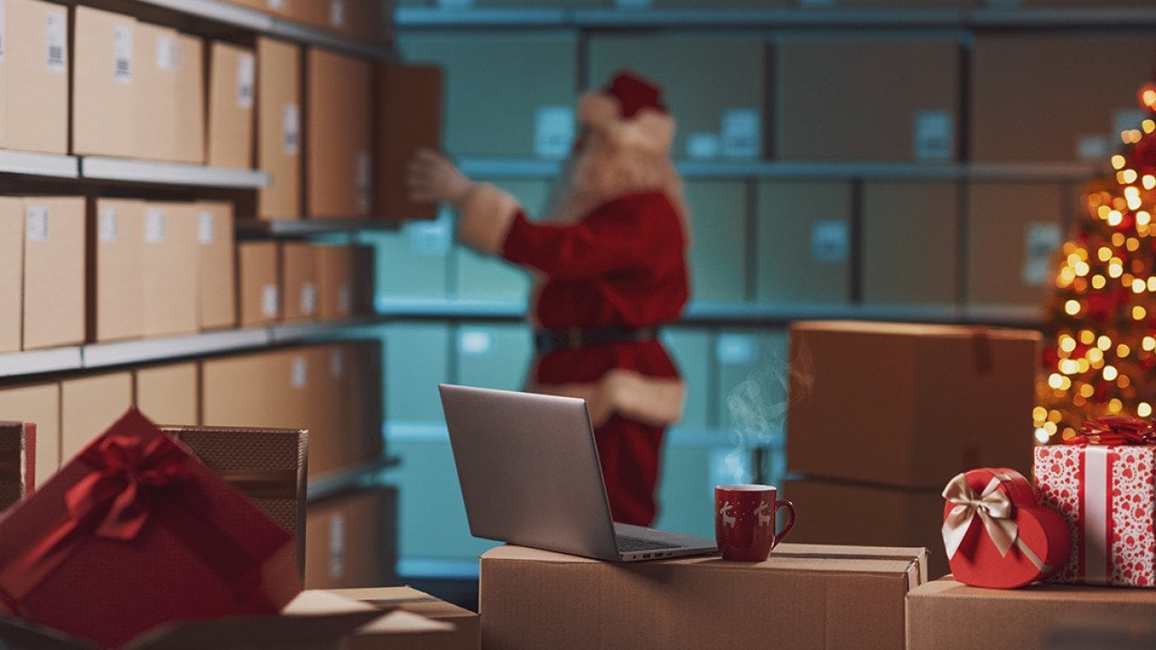 A worker dressed as Santa Claus prepares delivery Christmas gift boxes in a warehouse.