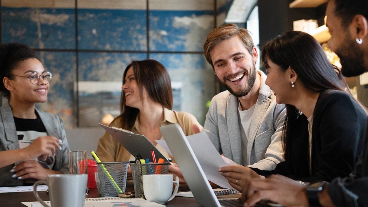 Five members of a business team talking together at a table with laptops open. 