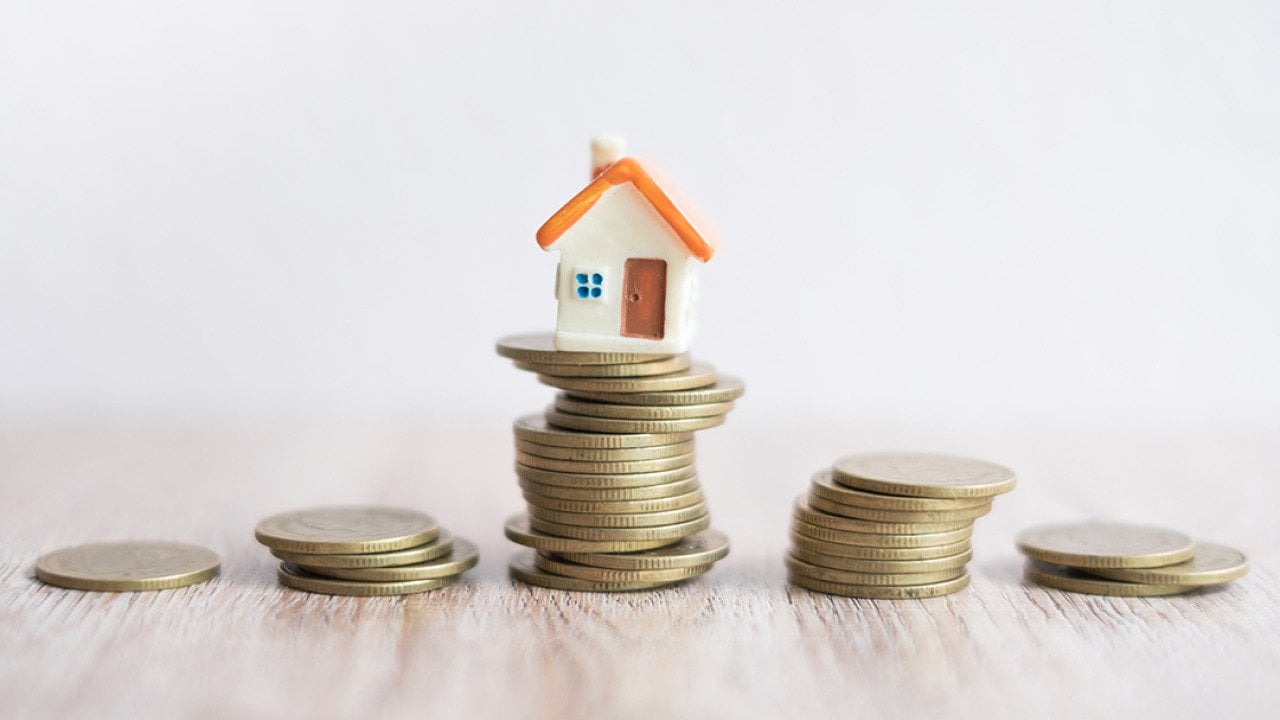 A miniature house on top of a stack of coins.