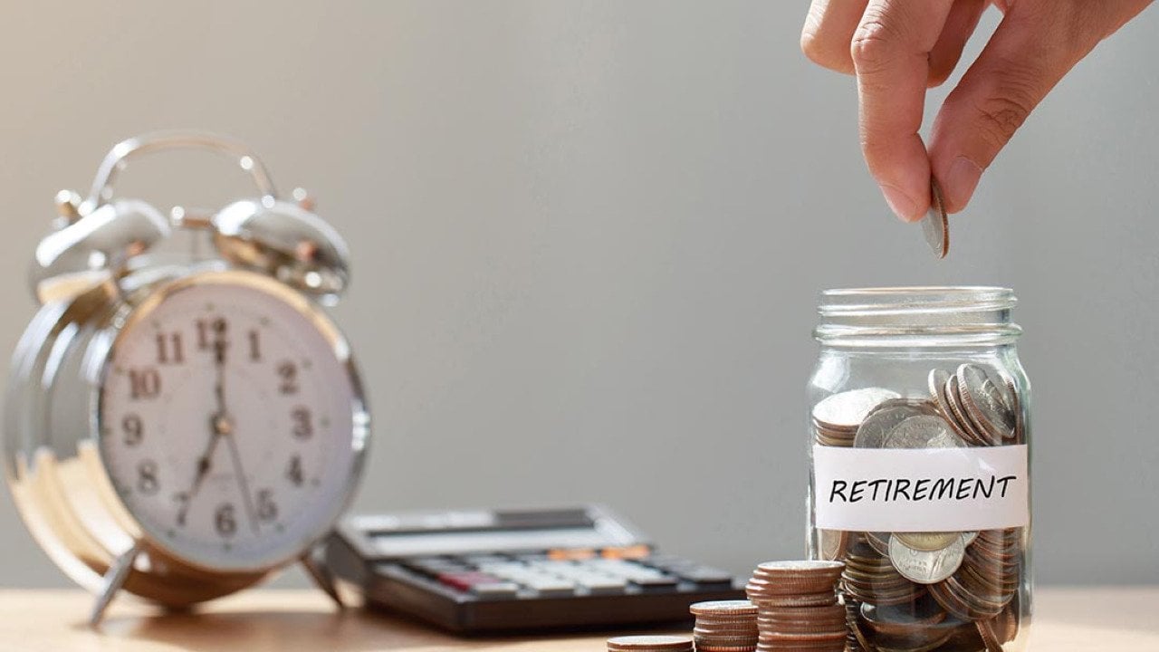 Hand putting coins in glass jar labeled