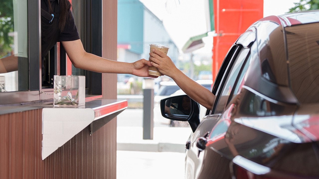 A customer picks up a cup of coffee and snack from a fast food drive-thru employee.