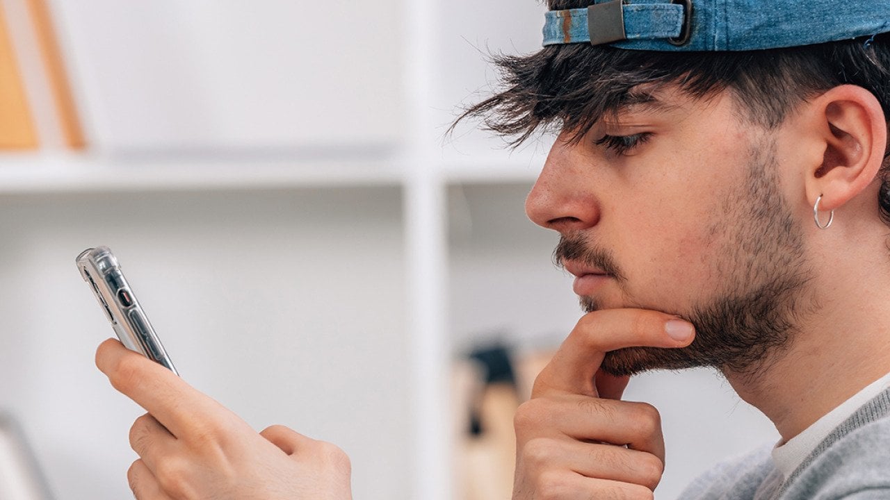 A young man looks at his smartphone pensively.