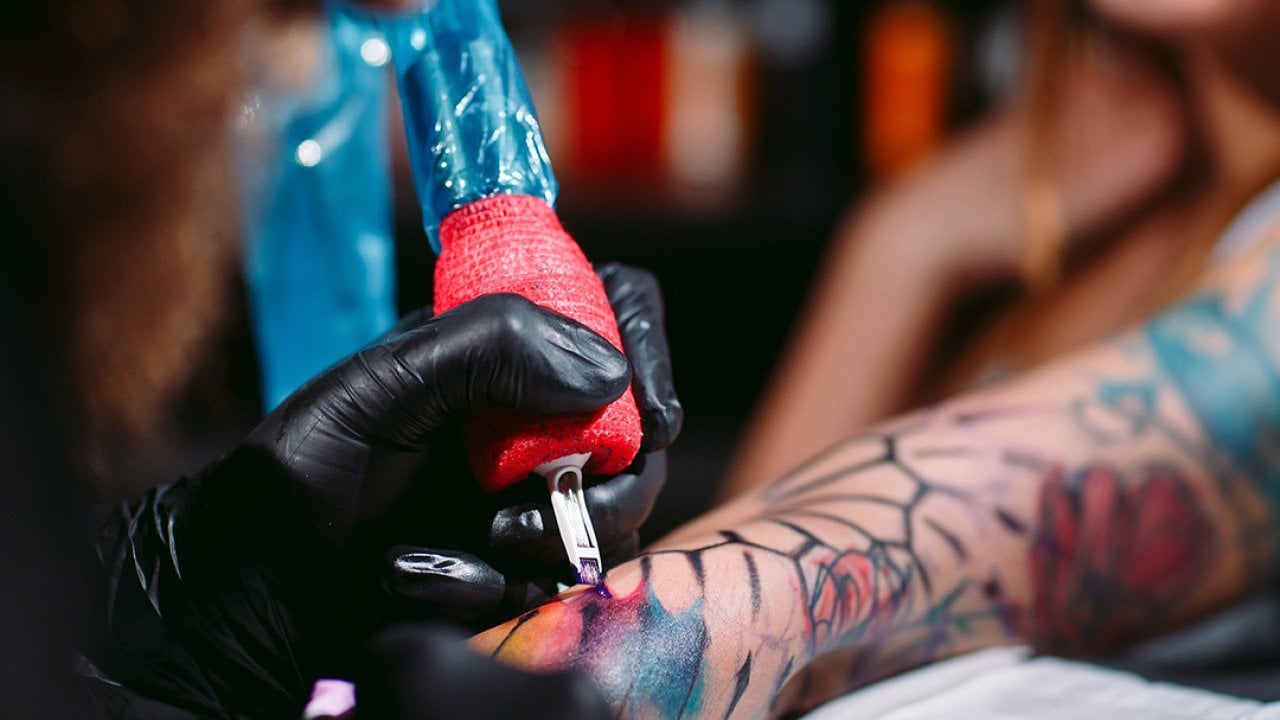 A professional artist tattooing a design on a woman's left forearm.