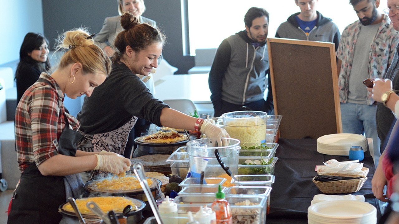 A catering team preparing food in front of awaiting employees.
