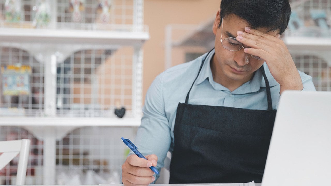 A male small business owner feeling stressful while reading finance documents.
