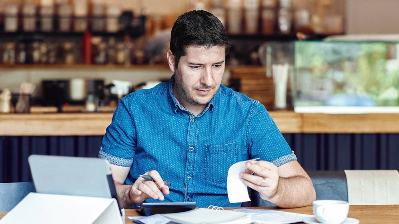 A male restaurant owner calculating business bills.