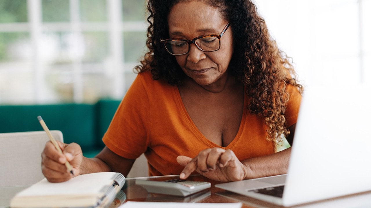 An elderly black woman calculating finances at home.