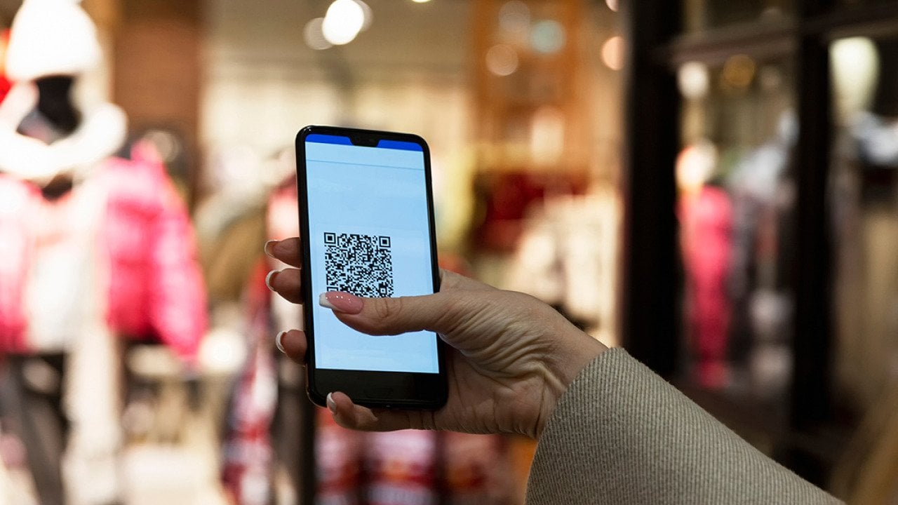 A person scans a QR code in a smartphone in front of a clothing store.