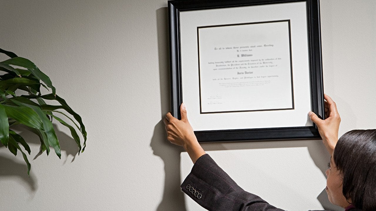 A business woman hanging a framed diploma.