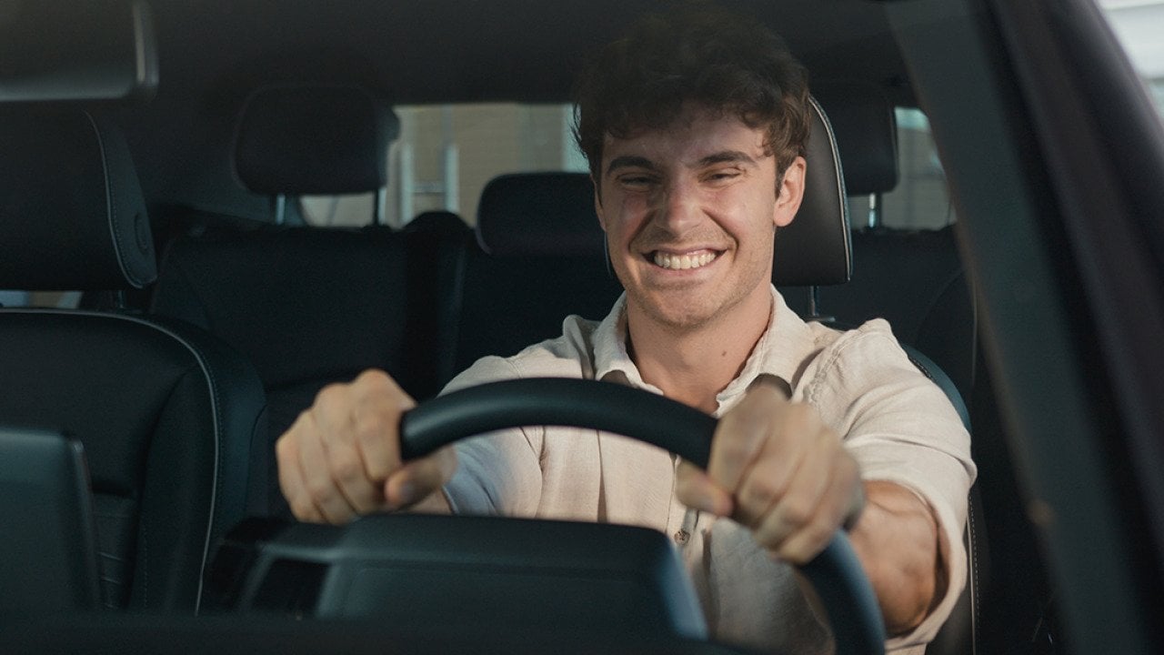 A young man with a big grin sits happily inside a new car.