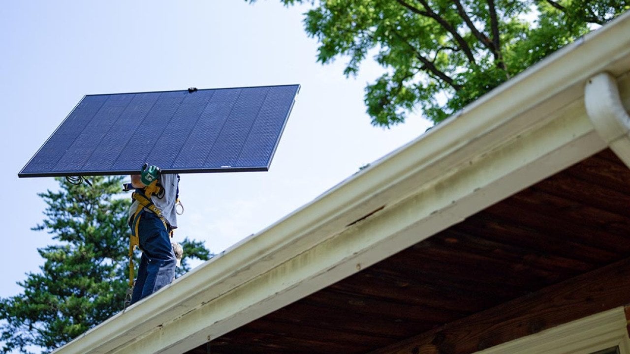 Michael Reimann, installer with Lumina Solar, carries a large panel and his face is not visible while installs solar panels on the roof of a home in Kensington, MD on July 3, 2025.