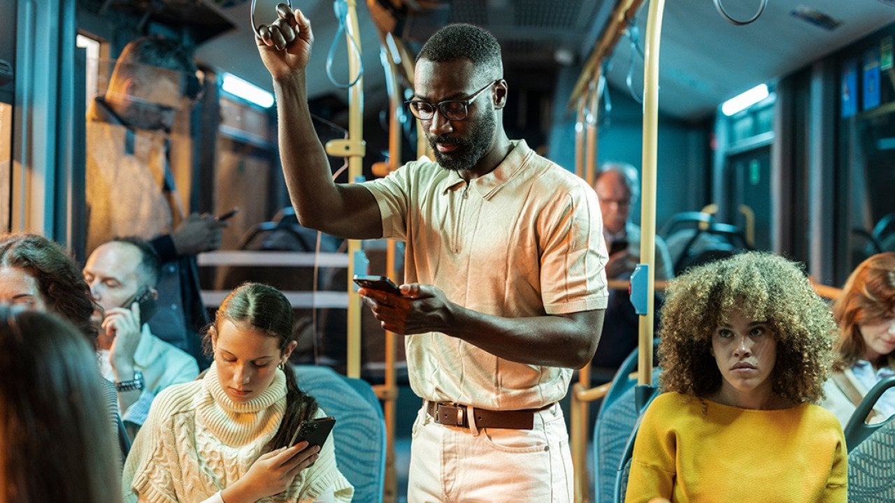 A young black man standing in a crowded bus at night.