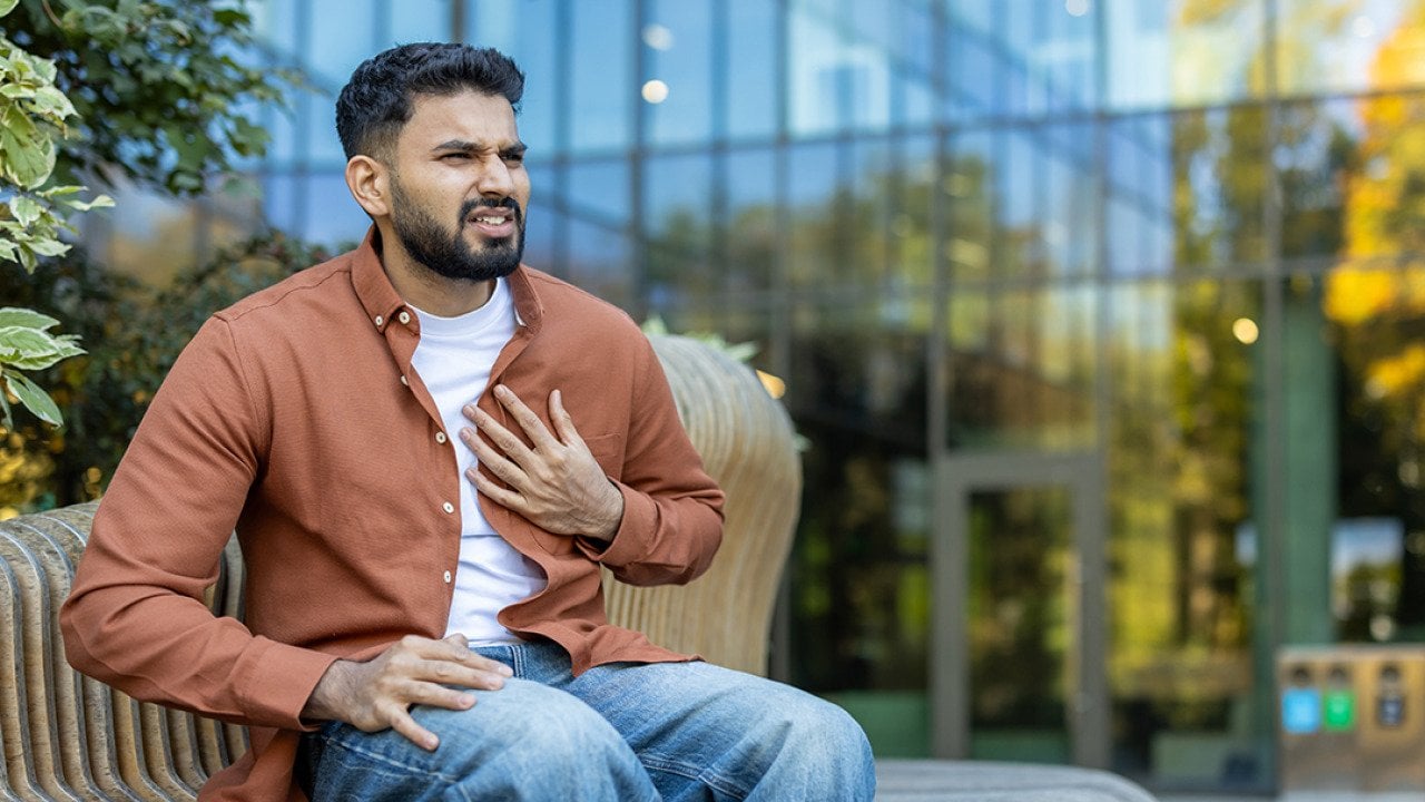 A young man nervously sitting on a bench outdoors experiencing chest pains.