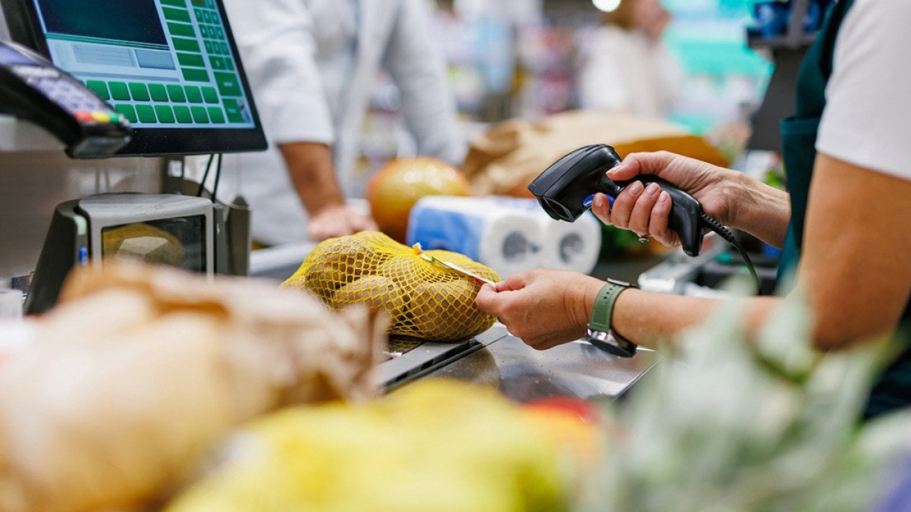 A supermarket cashier staff scans a bag of potatoes at a checkout counter.