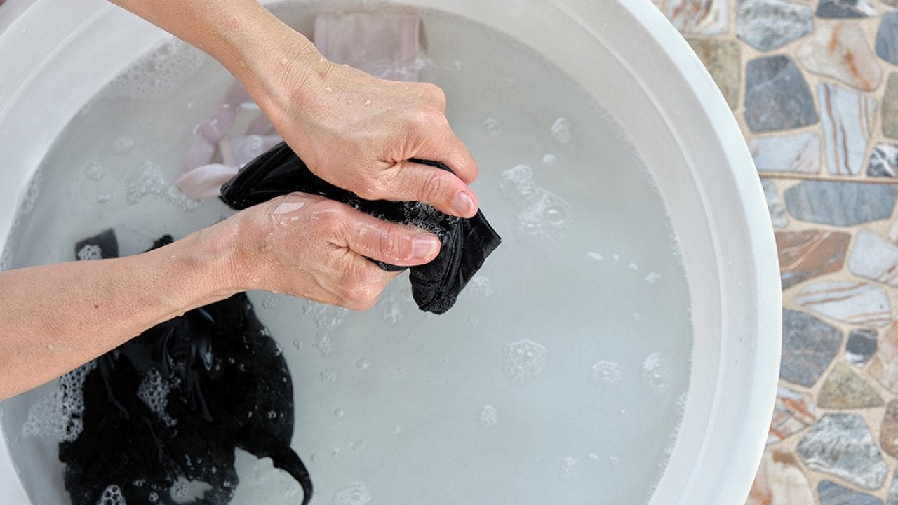 A couple of bras being hand-washed in a white basin.