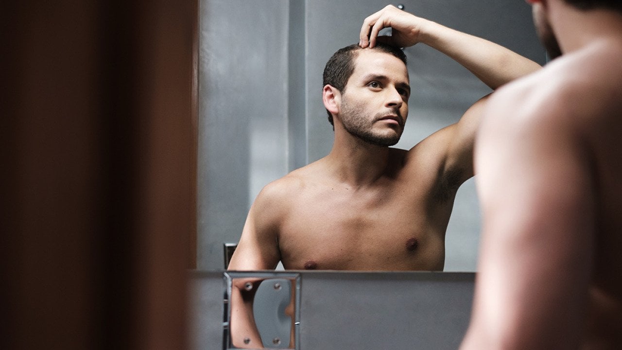 A man looks himself at the mirror inspecting his receding hairline.