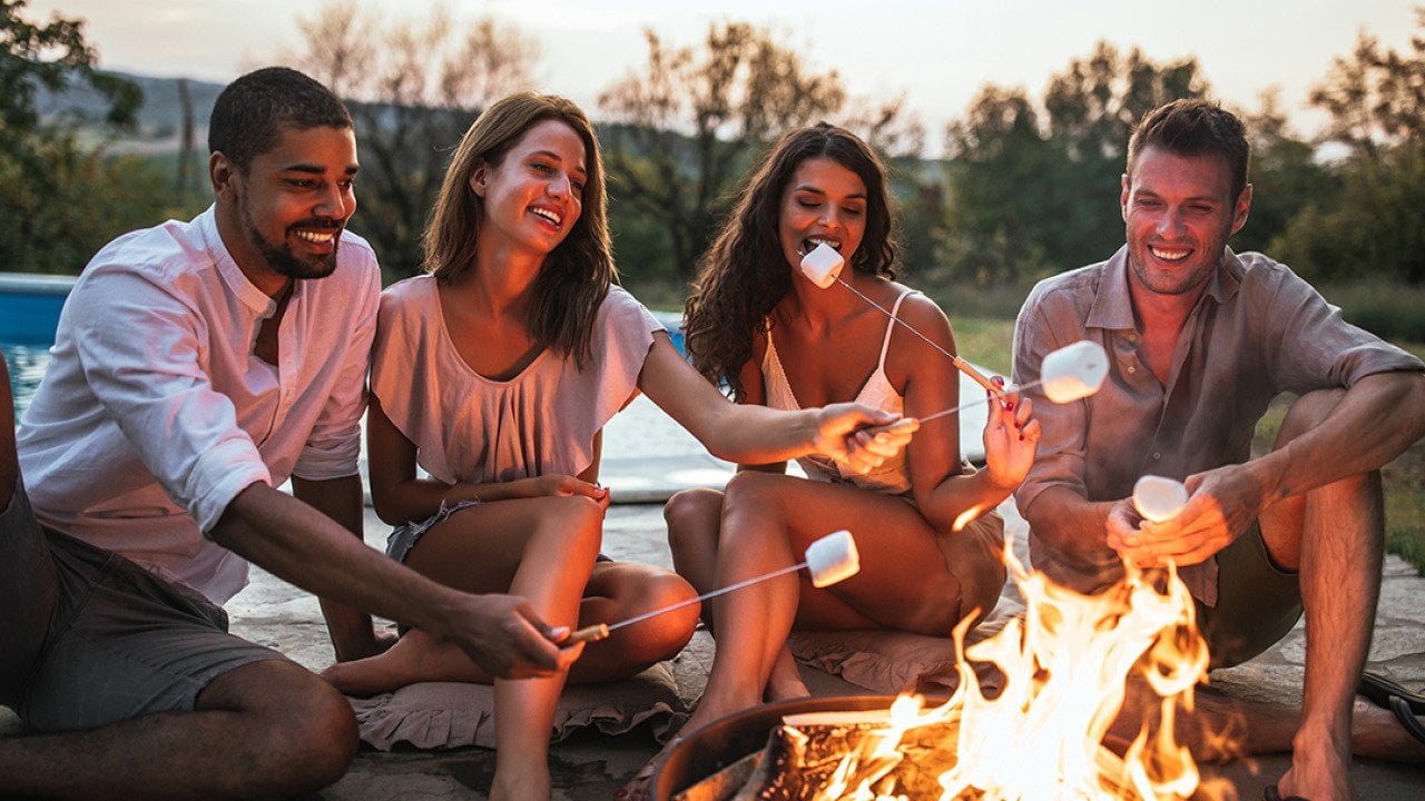 A group of four friends around a campfire grilling s'mores.