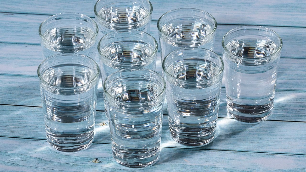 Eight glasses of water on a wooden table.
