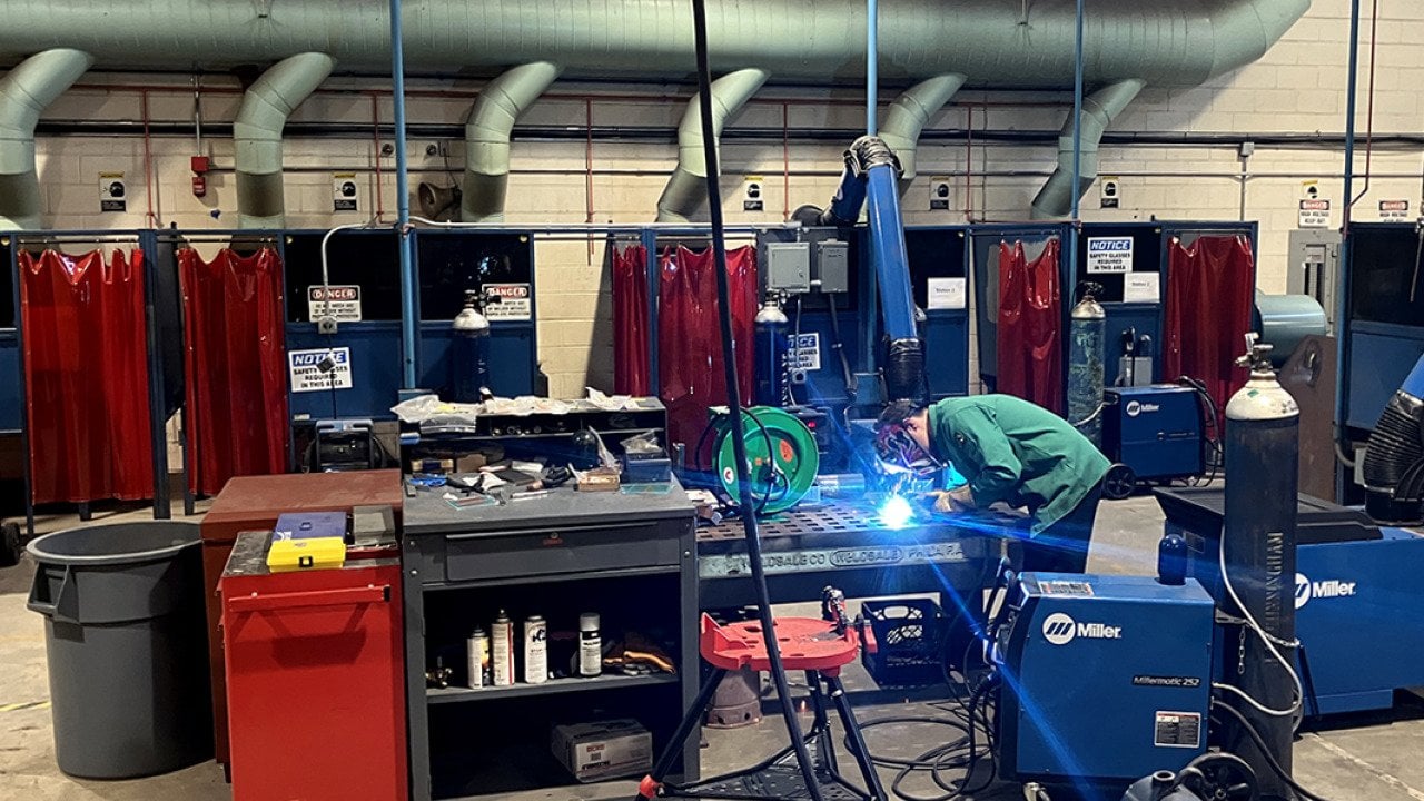 A welding demonstration taking place at a summer program in Philadelphia, colorful stations are in the background.