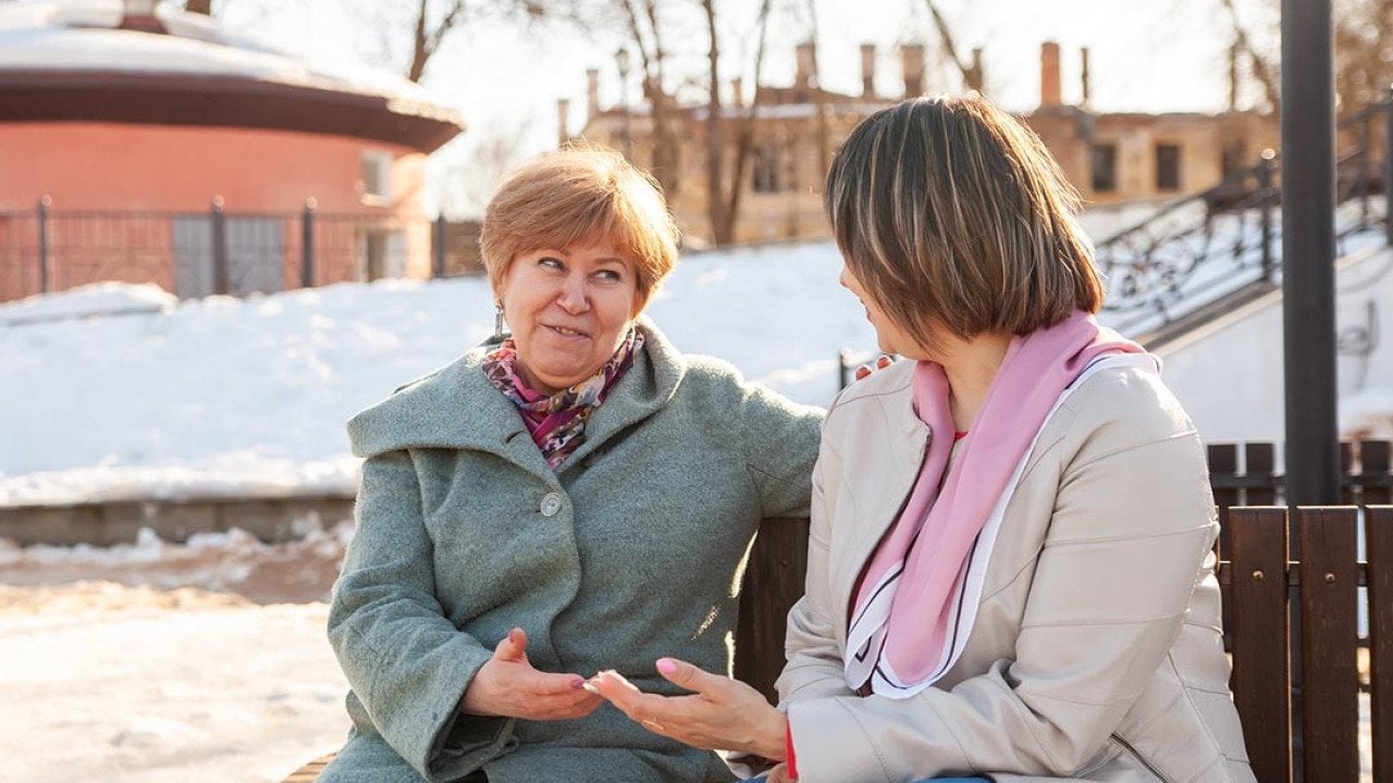 Contemplative casual middle-aged women sitting on bench winter, chatting.