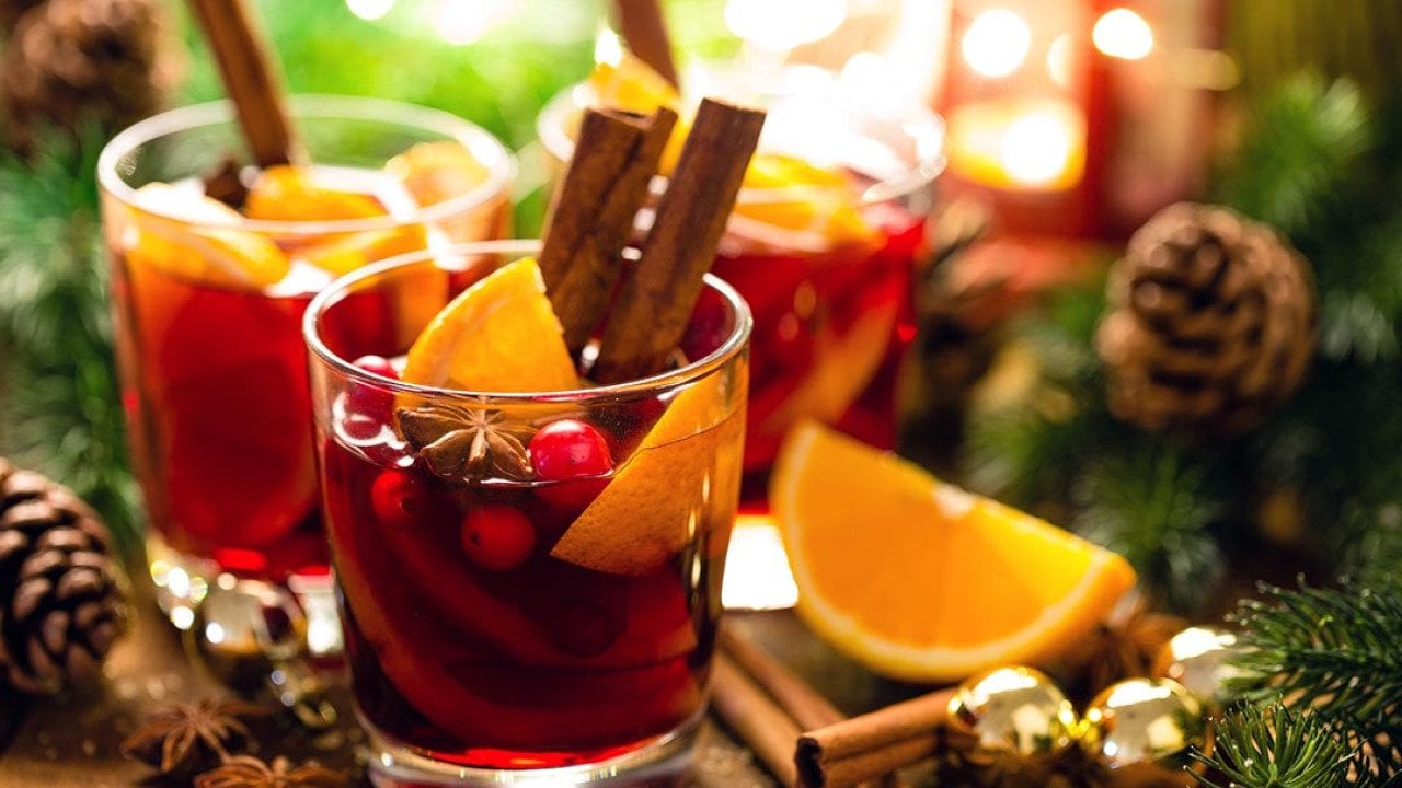 Christmas mulled red wine with spices and oranges on a wooden rustic table with evergreen decor and pine cones in the background.