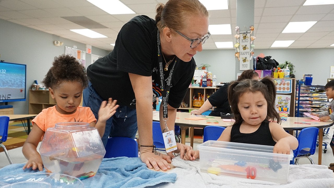 Head Start teacher Sasha Fair helps two preschool children with a science experiment.